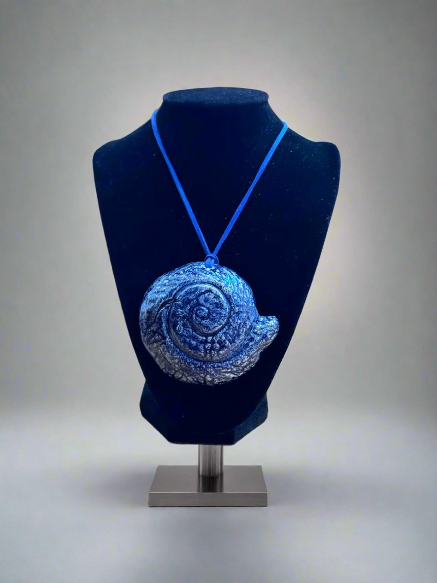 Medallón azul en forma de caracol marino de cerámica, exhibido en un busto de muestra