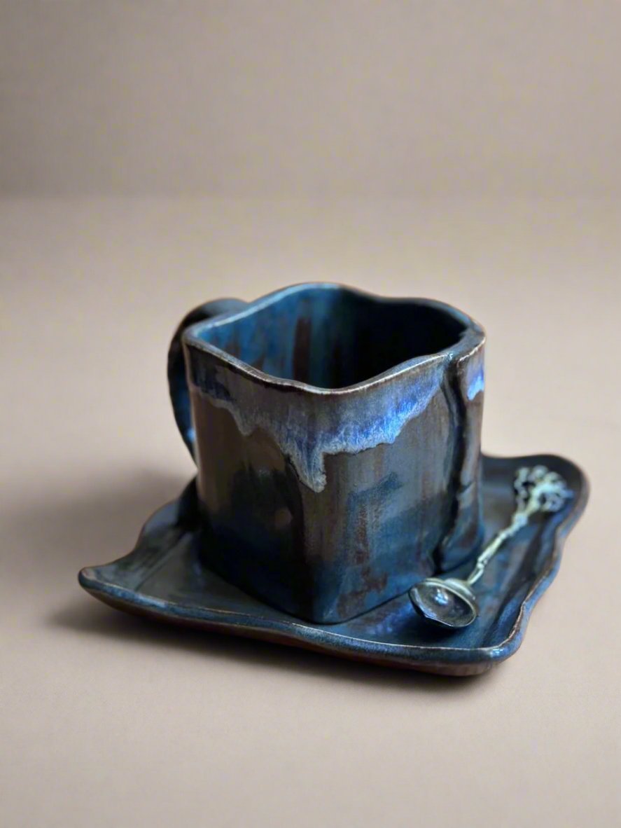 Taza cuadrada de cerámica azul oscuro con plato a juego, vista en ángulo